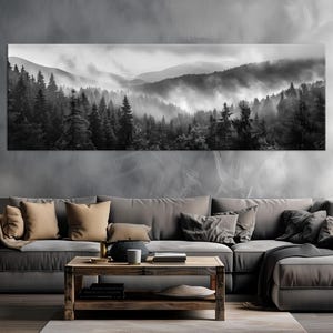 May include: A monochrome panoramic canvas print showing a misty forest scene. The artwork depicts a mountain range with dense evergreen trees and fog. The print is displayed above a grey sectional sofa with throw cushions and a wooden coffee table.