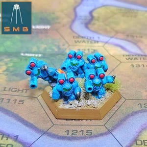 May include: A group of six blue and red miniature robots with guns, standing on a hexagonal base. The robots are posed in a battle formation, with their guns pointed forward. The base is made of brown plastic and has a textured surface.