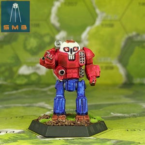 May include: A red and blue robot toy with a skull face and red eyes. The robot is standing on a hexagonal base.