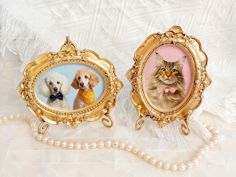 Two acrylic pet portraits in gold frames: one with a pair of white poodles in blue and yellow bandanas, the other with a Maine Coon cat wearing a pink bow