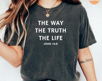 May include: Dark gray t-shirt with the text "THE WAY THE TRUTH THE LIFE JOHN 14:6" in white. The shirt has a crew neck and short sleeves. A gold necklace is visible. The shirt is made of a soft, comfortable material.