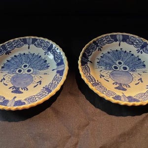 Può includere: Due piatti ovali in ceramica con un motivo floreale blu e bianco. I piatti hanno un bordo smerlato e un motivo centrale di una composizione floreale stilizzata. I piatti sono su una superficie scura.