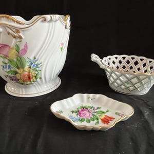 May include: Three white porcelain dishes with floral designs. The largest dish is a planter with a scalloped rim and a wavy design. The middle dish is a basket with a lattice design. The smallest dish is a shallow dish with a scalloped rim.