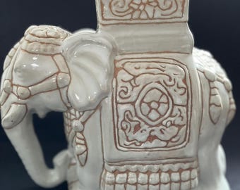 Puede incluir: Macetero de cerámica blanca en forma de elefante con intrincados diseños marrones. El macetero tiene una abertura cuadrada en la parte posterior para plantar.