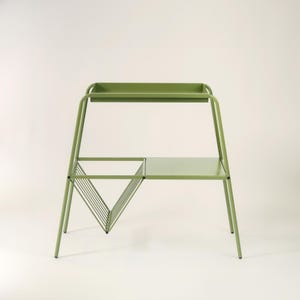 Puede incluir: Mesa auxiliar de metal verde claro con una bandeja superior, un estante inferior y un revistero triangular. La mesa tiene un diseño minimalista y es adecuada para uso en interiores. La mesa mide aproximadamente 76 cm de altura.