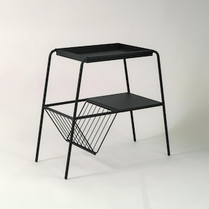 Peut inclure: Table d'appoint en métal noir avec plateau, étagère inférieure et porte-revues. La table a un design minimaliste avec un cadre géométrique et des pieds fins. La hauteur totale est d'environ 61 cm.