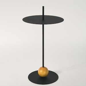 Könnte beinhalten: Ein schwarzer Beistelltisch aus Metall mit runder Tischplatte und einem Holzfuß.