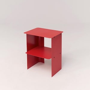 Könnte beinhalten: Ein leuchtend roter Beistelltisch mit zwei Ebenen. Der Tisch hat eine rechteckige Oberseite und ein unteres Regal, die beide von flachen, vertikalen Seiten getragen werden. Maße: ca. 46 cm hoch, 30 cm breit und 30 cm tief.
