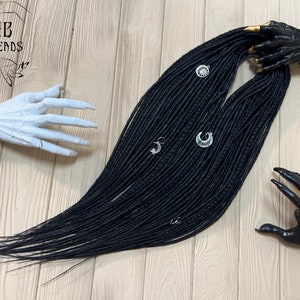 Puede incluir: Un conjunto de rastas sintéticas negras con abalorios plateados. Las rastas están dispuestas sobre una superficie de madera.