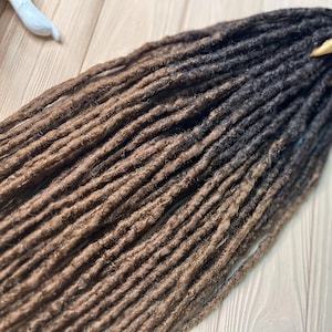 May include: A set of brown and black ombre synthetic dreadlocks. The dreadlocks are long and thick, and they are arranged in a neat pile. The dreadlocks are made of synthetic hair, and they are designed to be used as hair extensions.