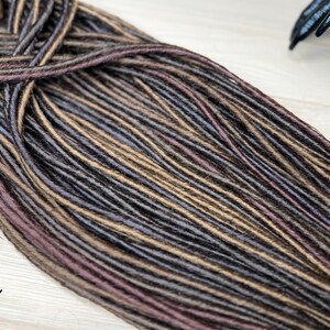 May include: A bundle of synthetic dreadlocks in shades of brown, gray, and purple. The dreadlocks are made of kanekalon hair and are ready to be installed.
