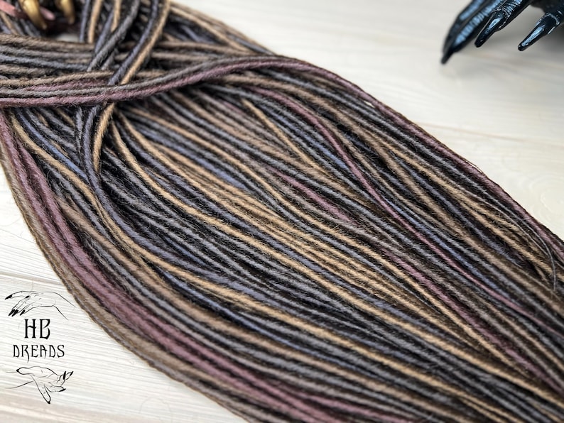 May include: A bundle of synthetic dreadlocks in shades of brown, gray, and purple. The dreadlocks are made of kanekalon hair and are ready to be installed.