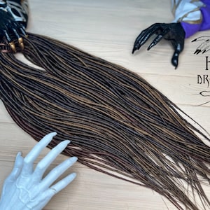 May include: A long set of brown and blonde synthetic dreadlocks. The dreadlocks are arranged in a straight line and are about 2 feet long.