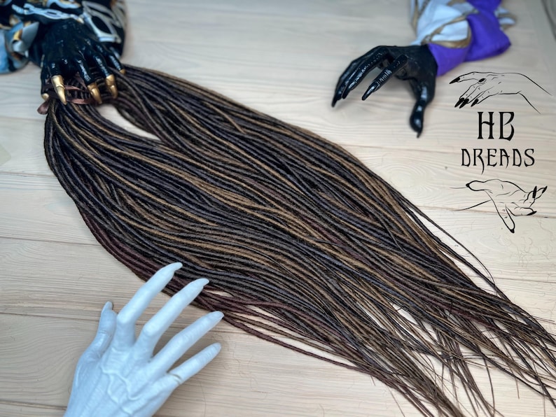 May include: A long set of brown and blonde synthetic dreadlocks. The dreadlocks are arranged in a straight line and are about 2 feet long.