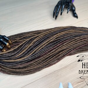 May include: A set of brown and black synthetic dreadlocks with a burgundy undertone. The dreadlocks are arranged in a long, flowing strand.