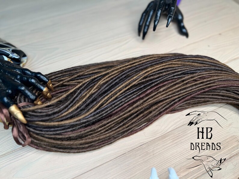 May include: A set of brown and black synthetic dreadlocks with a burgundy undertone. The dreadlocks are arranged in a long, flowing strand.