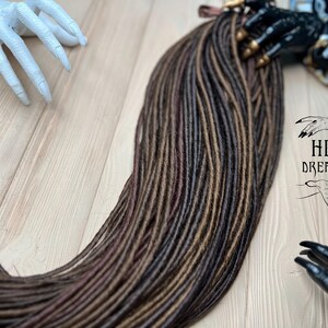 May include: A bundle of synthetic dreadlocks in brown, dark brown, and burgundy shades. The dreadlocks are arranged in a fan shape and are ready to be installed.