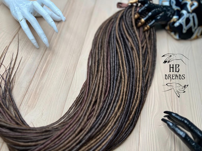 May include: A bundle of synthetic dreadlocks in brown, dark brown, and burgundy shades. The dreadlocks are arranged in a fan shape and are ready to be installed.