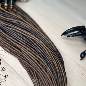 May include: A set of brown, black, and burgundy synthetic dreadlocks. The dreadlocks are arranged in a fan shape and are ready to be installed.