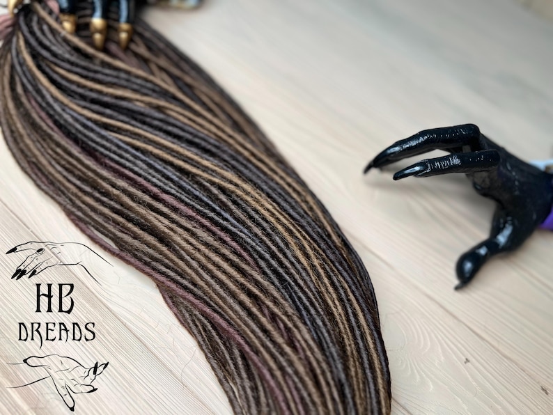 May include: A set of brown, black, and burgundy synthetic dreadlocks. The dreadlocks are arranged in a fan shape and are ready to be installed.