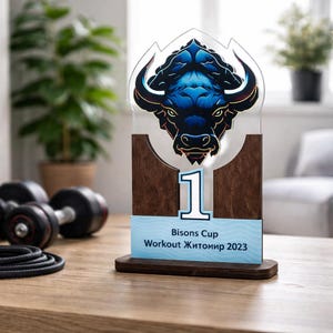 May include: A wooden trophy with a blue bison head design and the number 1. The trophy has a light blue banner that reads "Bisons Cup Workout Zhytomyr 2023". The trophy is on a wooden table.