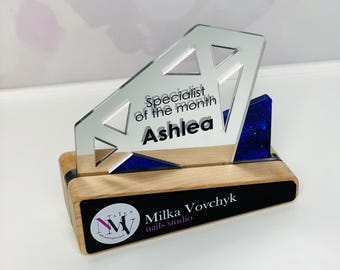 Puede incluir: Un premio de diamante plateado con una base azul y una inscripción negra que dice "Especialista del mes Ashlea". La base tiene una placa negra con el texto "Milka Vovchyk nails studio".