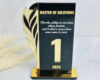 Puede incluir: Un premio acrílico negro y dorado con el texto "MASTER OF SOLUTIONS" y el número "1" en dorado. El premio también presenta el año "2025" y una cita sobre la resolución de problemas. Un diseño de hoja dorada está en el lado izquierdo.