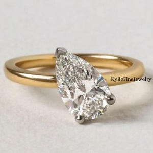 May include: A gold ring featuring a pear-cut diamond. The diamond is set with a silver-coloured metal and is the main feature of the ring. The ring band is a simple, polished gold.