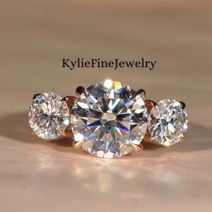 May include: A three-stone engagement ring featuring a large central diamond and two smaller diamonds on either side. The ring is set in rose gold.