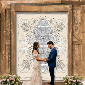 May include: A wedding ceremony with a couple holding hands in front of a large, ornate backdrop. The backdrop features a cream-colored design with black and white illustrations of trees, cats, and celestial symbols. The wooden door frame and floral arrangements add to the romantic setting.
