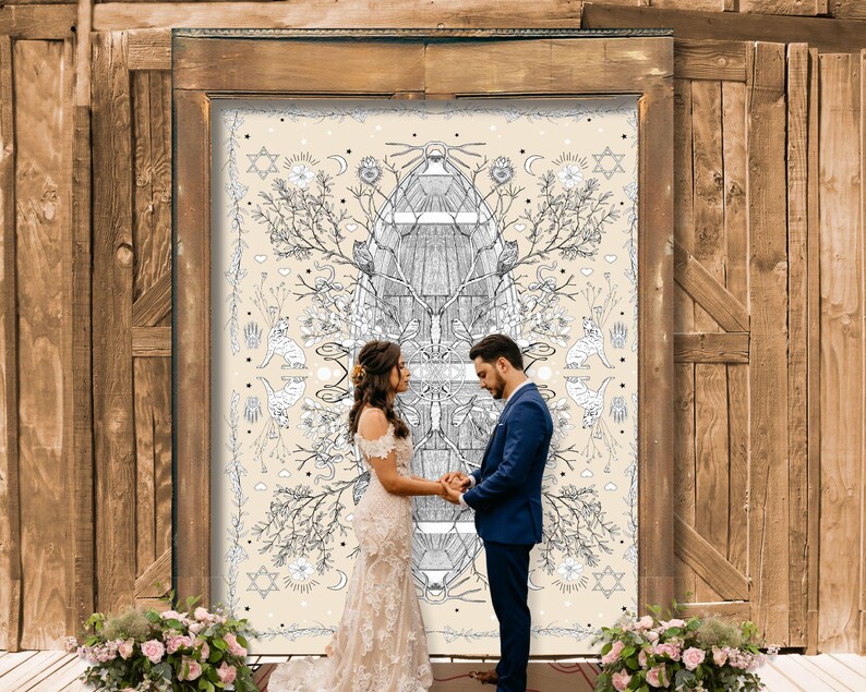 May include: A wedding ceremony with a couple holding hands in front of a large, ornate backdrop. The backdrop features a cream-colored design with black and white illustrations of trees, cats, and celestial symbols. The wooden door frame and floral arrangements add to the romantic setting.