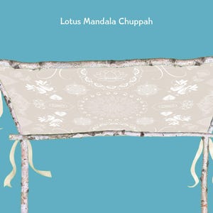 May include: A beige fabric chuppah with a lotus mandala design, supported by birch poles. The chuppah has cream-colored ribbons tied to the poles. The text "Lotus Mandala Chuppah" is at the top.