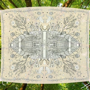 May include: A beige tapestry with a detailed black and white illustration of a symmetrical design featuring trees, animals, and celestial elements. The tapestry is suspended between two tree branches against a backdrop of a lush green forest.