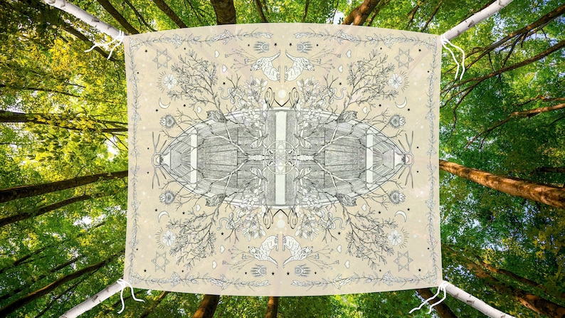 May include: A beige tapestry with a detailed black and white illustration of a symmetrical design featuring trees, animals, and celestial elements. The tapestry is suspended between two tree branches against a backdrop of a lush green forest.