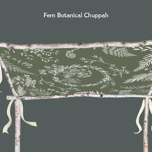 May include: A rustic birch wood chuppah with a green fabric backdrop. The fabric is adorned with white botanical fern and floral illustrations. Cream-colored ribbons hang from the frame. The text "Fern Botanical Chuppah" is at the top.