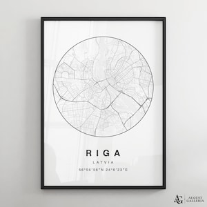 Op de afbeelding: Een zwart-witte kaartprint van Riga, Letland. De kaart bevindt zich in een cirkel met de naam van de stad en de coördinaten eronder. De print is ingelijst in een zwart frame.