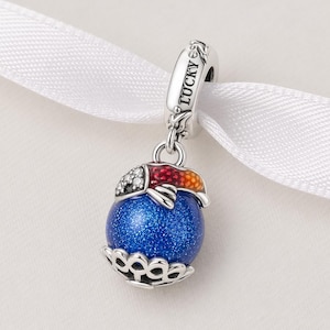 May include: A silver charm with a blue glittery orb, topped with a colorful fish design. The fish has red, orange, and white accents. The charm is suspended from a silver loop with the word "LUCKY" engraved on it.