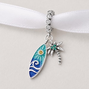 May include: A silver charm featuring a surfboard and palm tree. The surfboard is blue and turquoise with a yellow sun and wave design. The palm tree has green gem details.