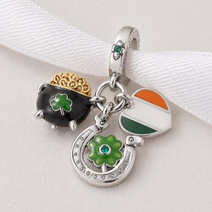 Op de afbeelding: Een zilveren bedel met hangers met het thema St. Patrick's Day. De bedel bevat een zwarte pot met goud, een groene klaver, een hoefijzer met een groene bloem en een hart met de kleuren van de Ierse vlag.