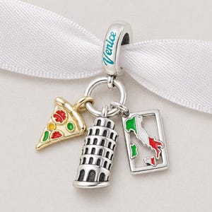 Può includere: Un charm d'argento con ciondoli a tema italiano. Il charm include una fetta di pizza, la Torre Pendente di Pisa e una mappa dell'Italia. La parola "Venice" è scritta in turchese sul charm.