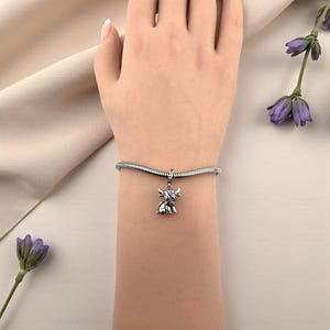 Puede incluir: Una pulsera con dije plateada con un dije de vaca de las Tierras Altas. El dije es detallado y cuelga de una pulsera de cadena de serpiente. La pulsera se usa en una mu&ntilde;eca, con un fondo suave y neutro.