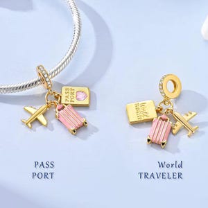May include: Two gold-colored travel charms with a suitcase, airplane, and passport design. One charm says "Pass Port" and the other says "World Traveler". The charms are attached to a silver bracelet.