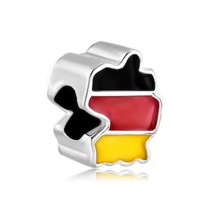 Puede incluir: Un charm plateado con la forma de Alemania, con los colores de la bandera alemana: negro, rojo y amarillo. El charm tiene una superficie pulida y reflectante, probablemente de metal.