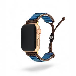 May include: A gold Apple Watch with a blue and brown beaded band. The band is made of small, round beads and has a brown cord with a knot at the end.