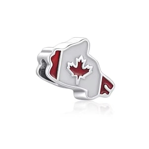Puede incluir: Un charm de plata con la forma de Canadá, con una hoja de arce roja y detalles rojos. El charm tiene un fondo blanco y probablemente está hecho de metal. El diseño es un símbolo patriótico.