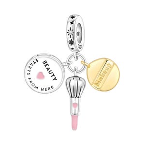 Könnte beinhalten: Ein silberner Charm mit Make-up-Motiv. Es zeigt einen Charm mit dem Text "BEAUTY STARTS FROM HERE", einen goldenen Charm mit dem Wort "Makeup", einen Make-up-Pinsel-Charm und einen sternenbesetzten Ring.