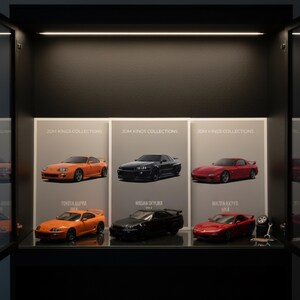May include: A display case featuring model cars. The case includes three panels with the text "JDM KINGS COLLECTIONS". Below the panels are miniature orange Toyota Supra, black Nissan Skyline, and red Mazda RX7 FD model cars. A wrench and tire are also visible.