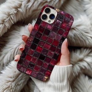 May include: A phone case with a mosaic tile design in shades of red, burgundy, and black. The case has a glossy finish and a camera cutout. The phone case is held in a person's hand.