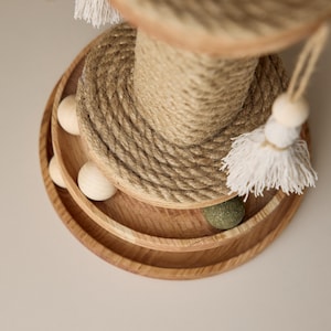 Peut inclure: Un griffoir pour chat en bois avec un poteau central recouvert de corde de sisal et trois étages. Le niveau supérieur a un pompon blanc qui pend. Le niveau intermédiaire a une boule en bois et le niveau inférieur a une boule verte.