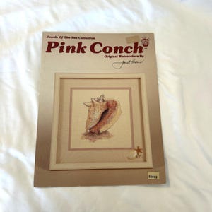 May include: A framed watercolor print of a pink conch shell, part of the "Jewels Of The Sea Collection." The artwork is signed by Janet Powers. A small starfish and shell are also depicted.